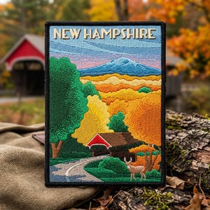 May include: A rectangular embroidered patch featuring the text NEW HAMPSHIRE at the top. The design depicts a landscape with a blue mountain, autumn-colored trees in shades of yellow and orange, a red-roofed covered bridge, and a deer.