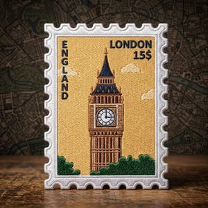 May include: A rectangular embroidered patch shaped like a postage stamp featuring a tan background with the text ENGLAND and LONDON 15$. The design depicts the Big Ben clock tower in brown and blue thread with green foliage at the base.
