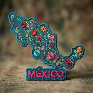 May include: A teal embroidered patch shaped like the map of Mexico, featuring colorful floral patterns in red, orange, pink, and light blue. The word MÉXICO is stitched in bold pink letters at the bottom of the patch with a scalloped teal border.