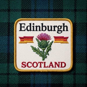 May include: A square embroidered patch with a white background and a gold border. The text Edinburgh is in black, and the text SCOTLAND is in red. A purple and green thistle flower is centered between two small orange and red ribbon banners.