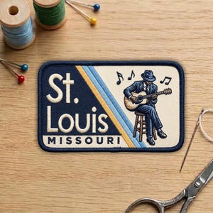 May include: Embroidered patch featuring a musician playing a guitar, with the text "St. Louis MISSOURI". The patch has a navy blue border and a cream-colored background with blue and yellow stripes.