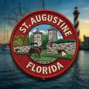 May include: A circular embroidered patch featuring a red border with the white text ST. AUGUSTINE FLORIDA and OLDEST CITY IN THE U.S. The center depicts a horse-drawn carriage, stone walls, and two towers against a blue sky and green landscape.