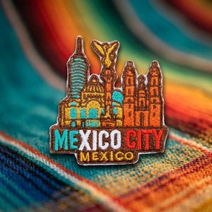 May include: An embroidered patch featuring a skyline of Mexico City landmarks in shades of brown, yellow, and teal. The text MEXICO CITY is stitched in teal, white, and red, with the word MEXICO below in yellow thread on a brown background.