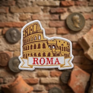 May include: An embroidered patch featuring a golden-brown depiction of the Colosseum in Rome. Below the structure, a white banner with a gold border displays the word ROMA in bold red capital letters. The patch has a white stitched border.