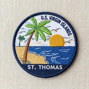 May include: A circular embroidered patch featuring a tropical beach scene with a palm tree, a yellow sun, and blue ocean waves. The text U.S. VIRGIN ISLANDS is arched at the top, and ST. THOMAS is printed in white at the bottom on a dark blue border.