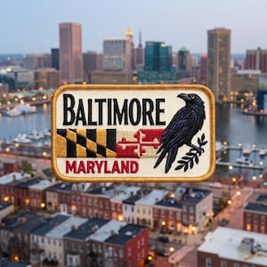 May include: A rectangular embroidered patch with a gold border on a cream background. It features the black text BALTIMORE above the Maryland state flag and the red text MARYLAND below. A black raven sits on a branch on the right side.