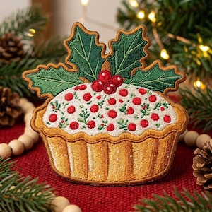 May include: An embroidered patch shaped like a holiday tart with a golden-brown crust, white icing, and red berries. The top is decorated with three large red berries and two dark green holly leaves with detailed stitching and brown borders.