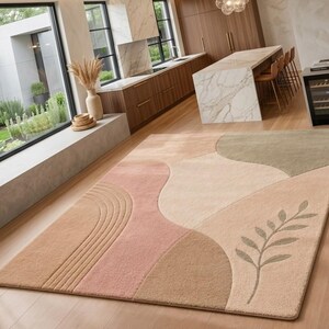 May include: A rectangular area rug featuring a soft color palette of beige, tan, dusty pink, and sage green. The design includes abstract curved shapes, a series of parallel lines on the left side, and a single botanical leaf motif on the right.