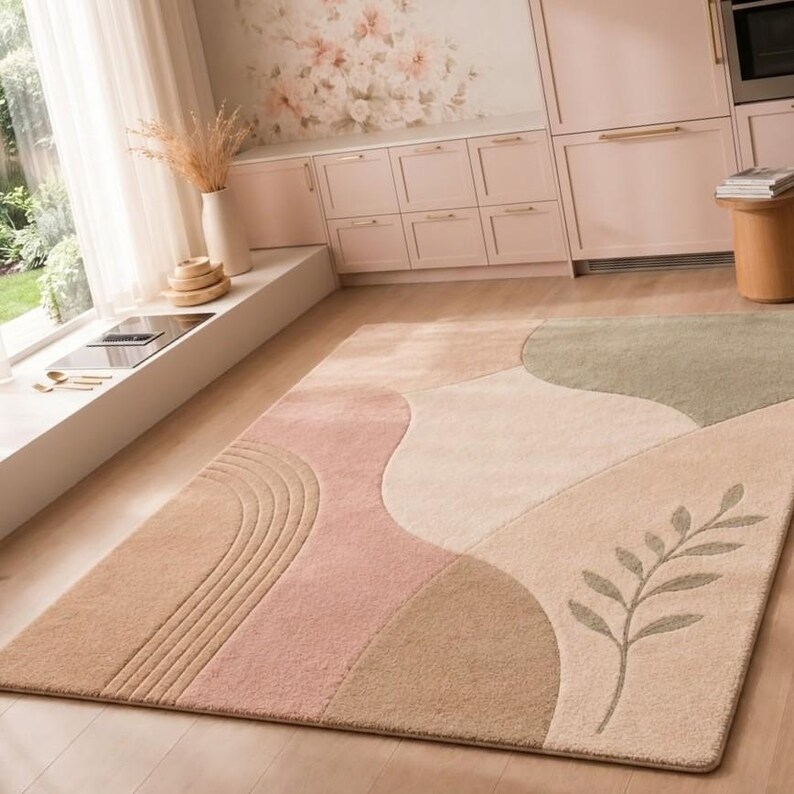 May include: A rectangular area rug featuring a soft, multi-colored abstract pattern with curved shapes in shades of beige, dusty pink, and sage green. The design includes a textured arch motif on one side and a delicate leaf branch illustration.