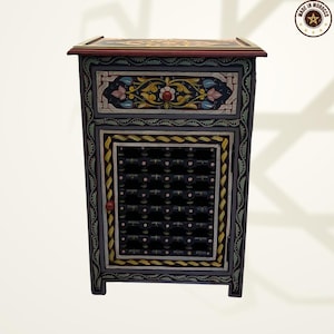 May include: A hand-painted, small wooden cabinet with intricate floral designs in yellow, blue, and pink on a dark background. The cabinet features a drawer and a door with a geometric pattern. The top is decorated with a floral border. Made in Morocco.