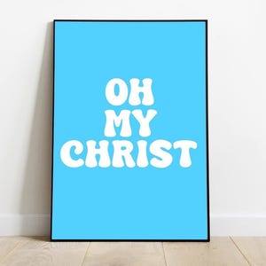 Może przedstawiać: Oprawiony wydruk artystyczny z jasnoniebieskim tłem i białym tekstem "OH MY CHRIST" w odważnej, retro czcionce. Wydruk jest w czarnej ramie i jest wyświetlany na białej ścianie i drewnianej podłodze.