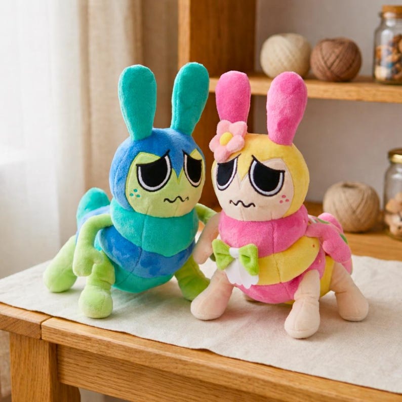 Puede incluir: Dos peluches h&iacute;bridos de oruga y conejo. Uno es azul y verde, el otro rosa y amarillo. Ambos tienen ojos grandes, bocas ca&iacute;das y orejas de conejo. El rosa y amarillo tiene una flor y un lazo.