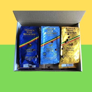Puede incluir: Caja de regalo abierta con tres paquetes de café Marley. Los paquetes son azules y dorados, con el texto "Jamaica Blue Mountain". Se ven granos de café. Fondo verde y amarillo.