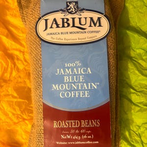 Puede incluir: Una bolsa de yute de café Jablum Jamaica Blue Mountain. La bolsa tiene una etiqueta azul y blanca con el texto "Jablum Jamaica Blue Mountain Coffee" y "Roasted Beans". La bolsa contiene 454 g de café.