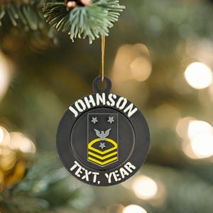 Peut inclure: Ornement de Noël noir avec le nom "JOHNSON" en lettres blanches. L'ornement présente un emblème militaire avec des étoiles, un oiseau et des rayures, et les mots "TEXT, YEAR". Il est suspendu à une ficelle dorée.