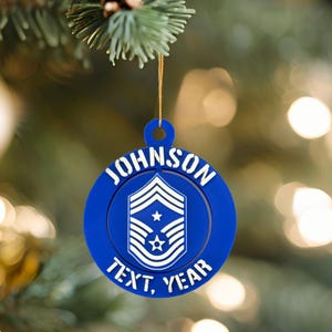 May include: A blue Christmas bauble with the name "JOHNSON" in white lettering. The bauble features a military insignia with stars and stripes, and the words "TEXT, YEAR" are also visible.
