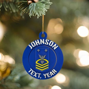 Puede incluir: Un adorno navideño azul con el nombre "JOHNSON" en letras blancas. El adorno presenta un emblema militar con estrellas y un águila, y también se muestran las palabras "TEXT, YEAR".