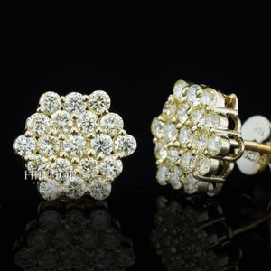 May include: A pair of gold stud earrings with a cluster of round, clear gemstones. The earrings have a hexagonal shape and are set against a black background. The text "HIP HOP" is visible on the left earring.
