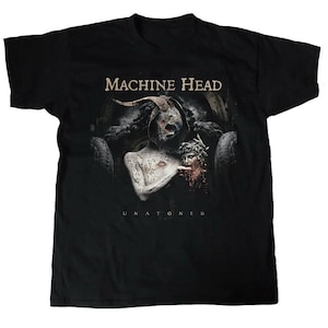 以下が含まれることがあります： 黒いTシャツ。バンド名「MACHINE HEAD」がセリフ体でプリントされ、その上にグラフィックが描かれています。グラフィックは角のある骸骨のような人物と、切断された頭部を持つ人物を描いています。「UNTONED」の文字が下にあります。