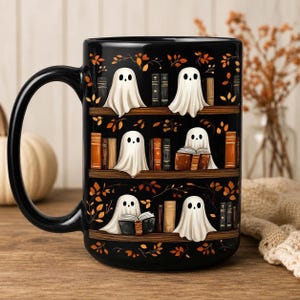 May include: A black ceramic mug featuring a repeating pattern of white ghosts sitting on wooden bookshelves among various books and scattered orange autumn leaves. The design wraps around the exterior of the mug, showcasing multiple ghosts reading books or resting on the shelves against a dark background.