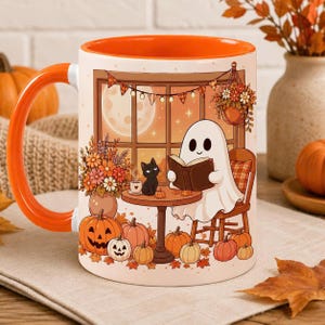 May include: A white ceramic mug with a bright orange handle and interior, featuring a colorful illustration of a ghost reading a book at a table with a black cat, surrounded by autumn flowers, pumpkins, and a window view of a full moon.