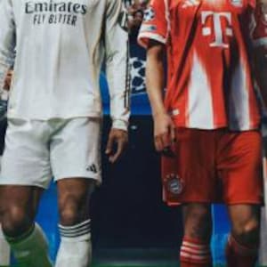 Puede incluir: Dos futbolistas con uniformes de equipo. Uno lleva una camiseta blanca de manga larga del Real Madrid con "Emirates FLY BETTER". El otro lleva una camiseta roja y blanca del Bayern de Múnich. Están en un campo verde.