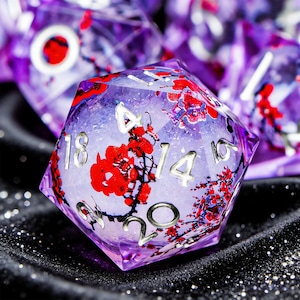 Puede incluir: Un dado de múltiples caras con un diseño de resina púrpura y transparente. El dado presenta detalles florales rojos y numeración plateada. El dado forma parte de un conjunto, con otros dados visibles en el fondo. Los dados están diseñados para juegos de mesa.