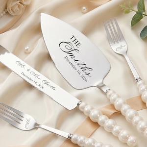 以下が含まれることがあります： 結婚式のケーキナイフ、サーバー、フォークのセット。 銀色の食器は、真珠のようなハンドルが付いています。 ナイフとサーバーには、結婚の日付とともに「Mr. & Mrs. Smiths」と「The Smiths」が刻印されています。 セットはサテンの表面にあります。