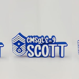 May include: A blue and white name tag with the text "CMSgt E=9 SCOTT". The tag features a military rank insignia with stars and stripes. The design is in a 3D style, suitable for military personnel.