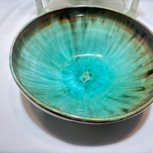 May include: A ceramic bowl with a turquoise and brown glaze. The bowl has a rounded shape with a slightly flared rim. The interior of the bowl is a vibrant turquoise color, while the rim and outer edges are a darker brown.