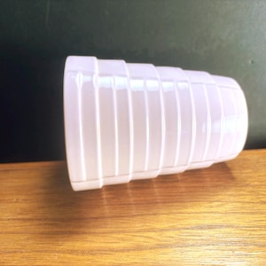 May include: A white, ribbed, cylindrical object with a rounded base and a wider top. The object is lying on a wooden surface, with a dark green and black background. The object appears to be a decorative item or a container.