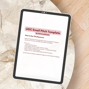 Peut inclure: Une tablette numérique affichant un "Modèle de Pitch par e-mail UGC" avec des instructions sur l'utilisation de la ressource. La tablette est sur une surface à motifs de marbre. Le texte comprend des invites pour les créateurs débutants.