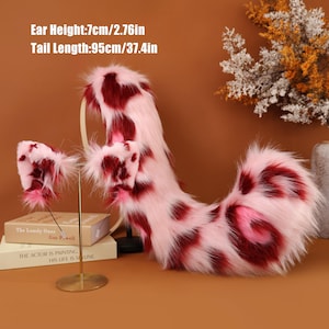 Puede incluir: Un conjunto de cola y orejas de gato de piel sintética rosa y burdeos. La cola mide 95 cm de largo y las orejas 7 cm de alto. El conjunto tiene un estampado moteado. El texto de la imagen dice: Altura de la oreja: 7 cm, Longitud de la cola: 95 cm.