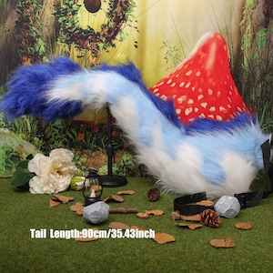May include: A blue, white, and light blue faux fur tail with a black belt. The tail is 90cm long. The tail is fluffy and has a gradient effect. The background includes a red mushroom with white spots and decorative elements.