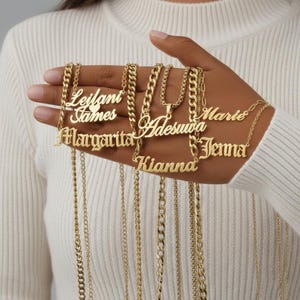 以下が含まれることがあります： 「Leilani」「James」「Margarita」「Adesuwa」「Marie」「Kianna」「Jenna」などの名前が刻まれた、ゴールドカラーのネームネックレス。チェーンは様々なスタイル。名前はエレガントなフォントで書かれています。
