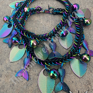 May include: Two mermaid-themed necklaces. The chainmail-style necklaces are black with iridescent blue, green, and purple accents. Each necklace features mermaid tail and scale charms, along with iridescent bell charms.