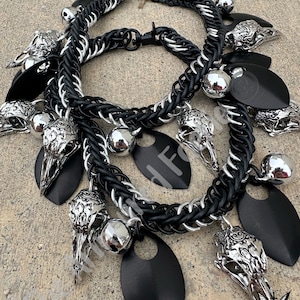 May include: Two necklaces with a gothic theme. The necklaces are made of black and silver chainmail, adorned with silver raven skull pendants, black teardrop-shaped charms, and silver ball charms. The necklaces are displayed on a neutral surface.