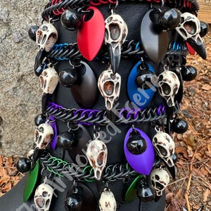 May include: Black boot adorned with decorative chainmail and pendants. The pendants include bird skull charms, black spheres, and colorful teardrop-shaped accents in red, black, blue, green, and purple. The boot is decorated with chainmail in red, black, blue, green, and purple.