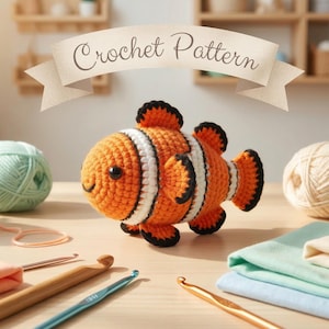 May include: An orange, black, and white crocheted clownfish sits on a wooden surface, surrounded by yarn balls in various colors, crochet hooks, and fabric. The banner above reads "Crochet Pattern".