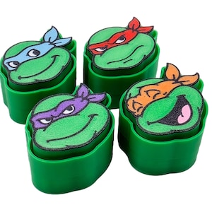 May include: Four green containers with Teenage Mutant Ninja Turtle character faces. Each turtle has a different colored mask: blue, red, purple, and orange. The containers are green and have a rectangular shape.