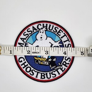 Peut inclure: &Eacute;cusson brod&eacute; Ghostbusters, d'environ 10 cm de diam&egrave;tre. L'&eacute;cusson pr&eacute;sente un fant&ocirc;me blanc, les mots "Massachusetts Ghostbusters" et un graphisme bleu et noir du logo Ghostbusters.