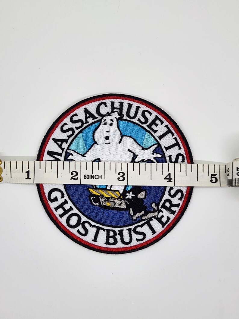 Peut inclure: &Eacute;cusson brod&eacute; Ghostbusters, d'environ 10 cm de diam&egrave;tre. L'&eacute;cusson pr&eacute;sente un fant&ocirc;me blanc, les mots "Massachusetts Ghostbusters" et un graphisme bleu et noir du logo Ghostbusters.