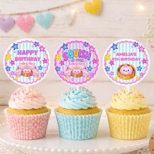 May include: Three cupcakes with pink, blue, and yellow frosting in polka-dot liners. Each has a round paper topper featuring light blue stripes, colorful stars, and illustrations of dim sum. Text reads Happy Birthday, Squish On Over, and Amelia's 6th Birthday.
