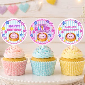 May include: Three cupcakes with pink, blue, and yellow frosting in matching polka-dot liners. Each cupcake is topped with a circular paper topper featuring a cartoon dumpling in a steamer, blue stripes, and colorful stars with text.