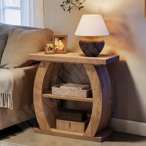 May include: A wooden side table with a lamp, two framed pictures, and storage baskets. The lamp has a white shade and a dark brown base. The table is made of light-coloured wood and has a curved design.