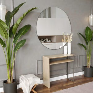 May include: A contemporary interior with a circular mirror on a grey wall. Below the mirror is a light wood console table with a metal frame, two white vases, and decorative plants. Potted plants flank the console table, creating a balanced aesthetic.