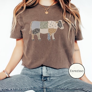May include: A brown short-sleeve t-shirt featuring a graphic of a cow composed of various patchwork patterns including blue gingham, floral prints, and stripes. A circular label in the bottom right corner displays the text Espresso.