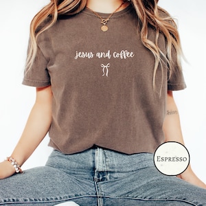 Op de afbeelding: Bruin T-shirt met de tekst "jesus and coffee" in een scriptlettertype en een strik-afbeelding. Het shirt wordt gecombineerd met een blauwe jeans. In de rechterbenedenhoek staat een kleurstalen met de naam "Espresso".