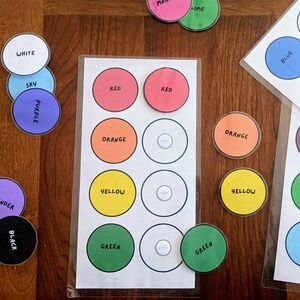 May include: A set of educational color matching cards featuring laminated white sheets with circular outlines and corresponding colored circular tokens. Each token and card space is labeled with text including red, orange, yellow, green, blue, purple, white, black, sky, lavender, maroon, and lime.