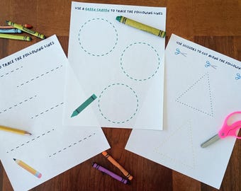 Puede incluir: Tres hojas de actividades blancas con líneas discontinuas negras para ejercicios de trazado y corte. Las hojas incluyen instrucciones de texto, como Use a pencil to trace the following lines, Use a green crayon to trace the following lines y Use scissors to cut along the following lines, acompañadas de varios crayones, un lápiz y tijeras rosas.
